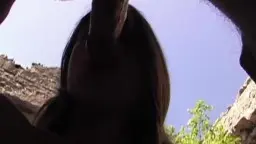 Geile Frau mit offenem Mund saugt tief im Freien an einem Schwanz, Hintergrund aus alten Steinmauern und blauem Himmel.
