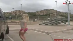 Blonde Frau in pinkem Rock vor Parkplatz mit Auto