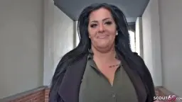 Ashley läuft mit offenem Mantel selbstbewusst durch eine urbane Gasse am Fluss