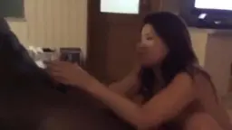 Japanerin kniet nackt auf dem Bett und saugt hingebungsvoll an einem riesigen schwarzen Schwanz