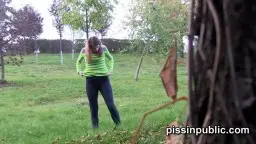 Junge Brünette in grünem Shirt spreizt die Beine und pinkelt im Park auf die Wiese