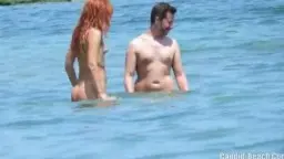 Nackte reife Frau und junger Mann stehen eng aneinander im flachen Meerwasser