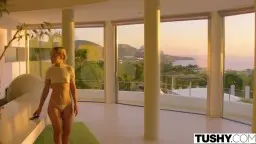 Blonder Model mit Zöpfen steht in engen Jeans auf Terrasse am Meer und zeigt ihren prallen Po einem Mann im weißen Hemd